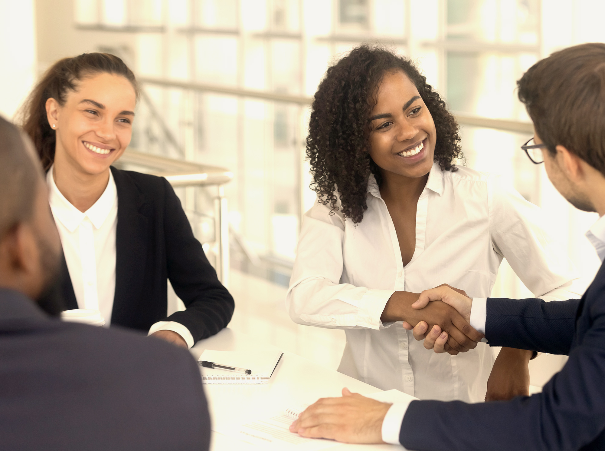  A black woman shakes hands with a man while another man and woman look on during a negotiation meeting with an insurance company representative.