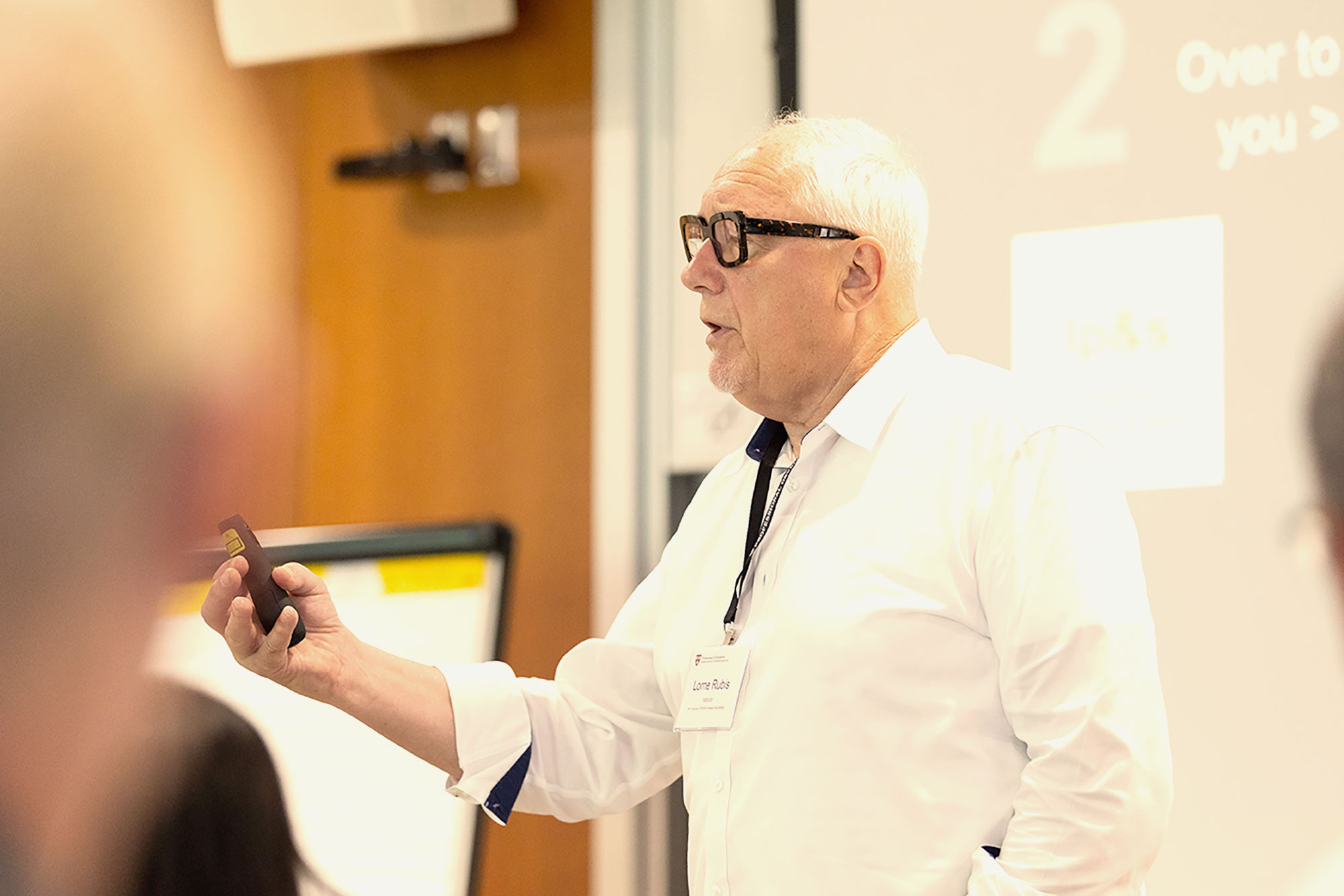 PDP Instructor Lorne Rubis stands at the front of a classroom holding a remote.